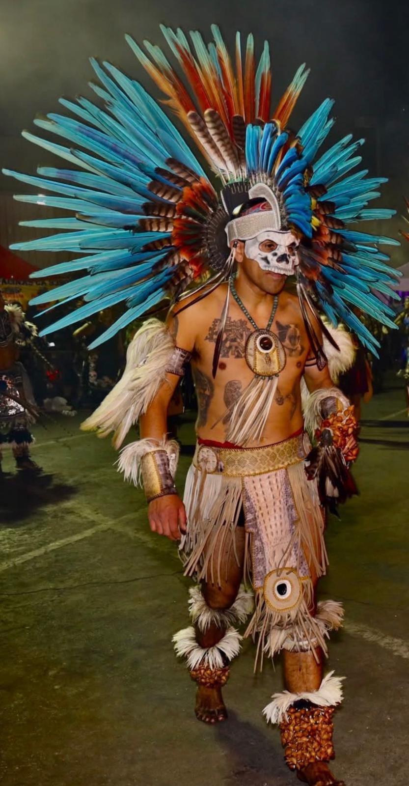 Male Aztec dancer in full blue feathered headdress with skull mask at night